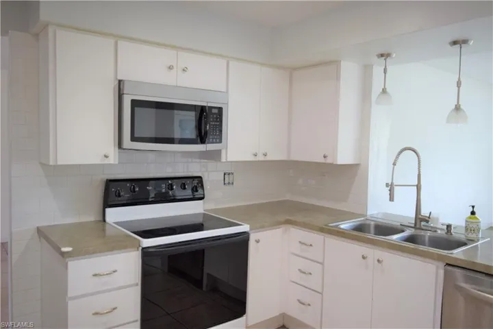 Kitchen with appliances with stainless steel finishes, white cabinets, backsplash, light countertops, and hanging light fixtures