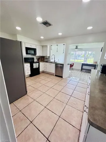 Kitchen with black appliances, white cabinetry, dark countertops, light tile patterned flooring, and recessed lighting