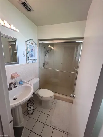 Full bath with light tile patterned flooring, tile walls, a stall shower, and wainscoting