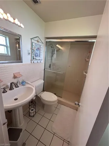 Bathroom featuring light tile patterned floors, tile walls, a stall shower, and a wainscoted wall
