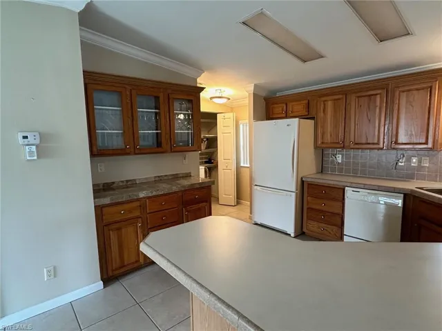 Kitchen featuring decorative backsplash, light tile patterned floors, crown molding, and white appliances