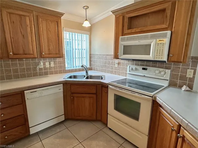Kitchen with light tile patterned floors, backsplash, white appliances, and sink