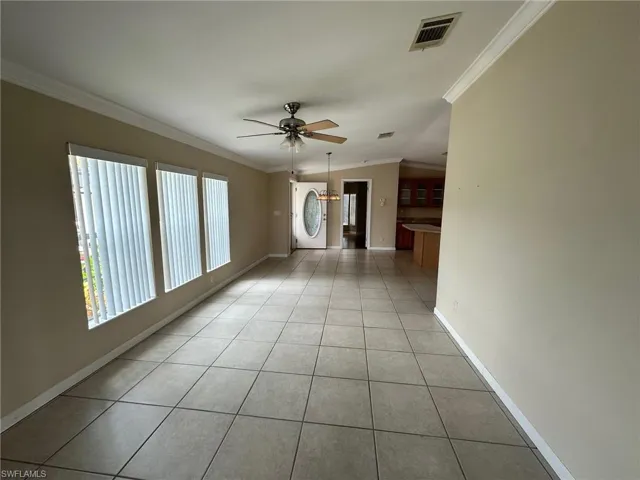 Tiled empty room featuring stacked washer and dryer, ornamental molding, and ceiling fan