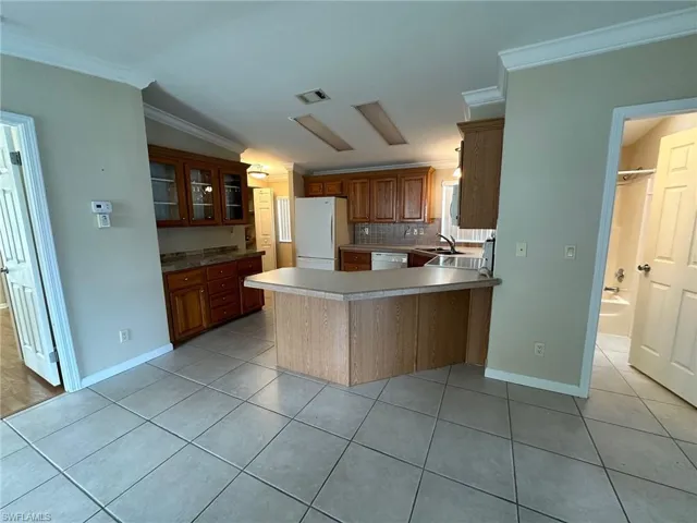 Kitchen with crown molding, kitchen peninsula, white appliances, and backsplash