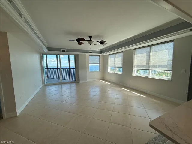 Living room with expansive views, coffered ceiling, light tile floors, crown molding, and a ceiling fan
