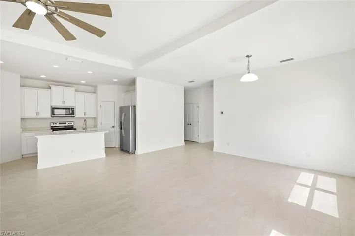 Unfurnished living room with a ceiling fan, visible vents, a sink, baseboards, and recessed lighting