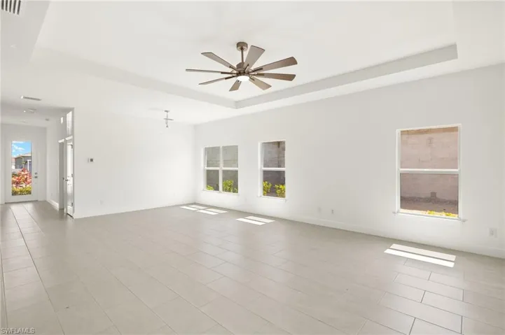 Empty room featuring baseboards, ceiling fan, light tile patterned floors, and a tray ceiling
