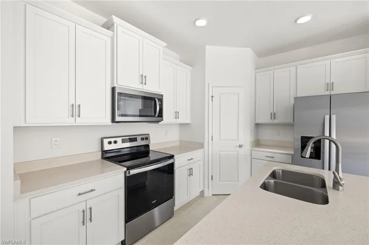 Kitchen featuring white cabinets, light stone countertops, appliances with stainless steel finishes, a sink, and recessed lighting