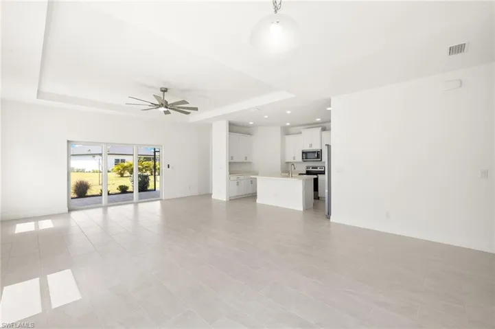 Unfurnished living room with ceiling fan, visible vents, a sink, baseboards, and a tray ceiling