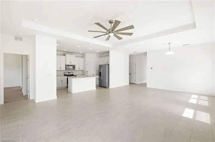 Unfurnished living room featuring a sink, a tray ceiling, visible vents, and ceiling fan