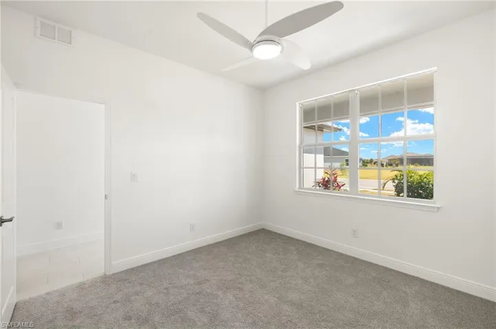 Carpeted empty room with ceiling fan, visible vents, and baseboards
