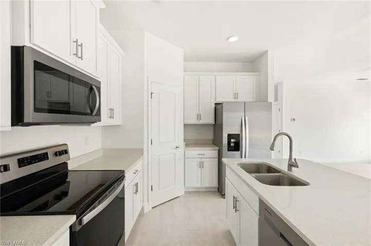 Kitchen with recessed lighting, white cabinetry, light stone counters, a sink, and stainless steel appliances
