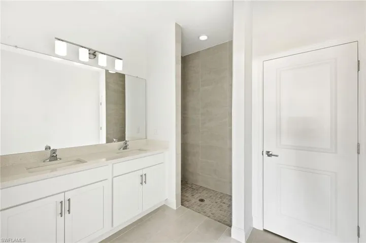Full bath with a sink, tile patterned flooring, a tile shower, and double vanity
