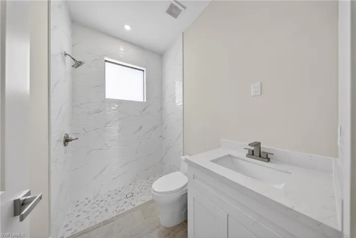 Walk-in shower with full-height white marble-look tile, rainfall showerhead, and window