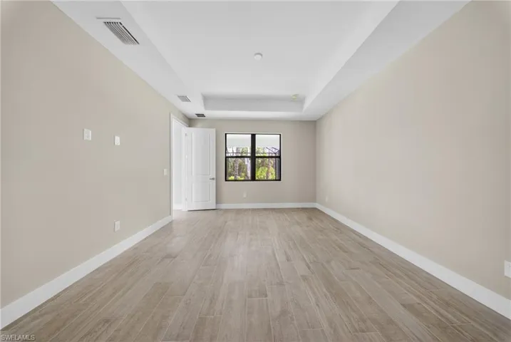 Spacious room featuring wood-finish tile flooring, neutral wall tones, and a tray ceiling with recessed lighting