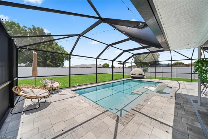 Screened enclosure featuring an in-ground swimming pool with an integrated sun shelf and surrounding paver patio