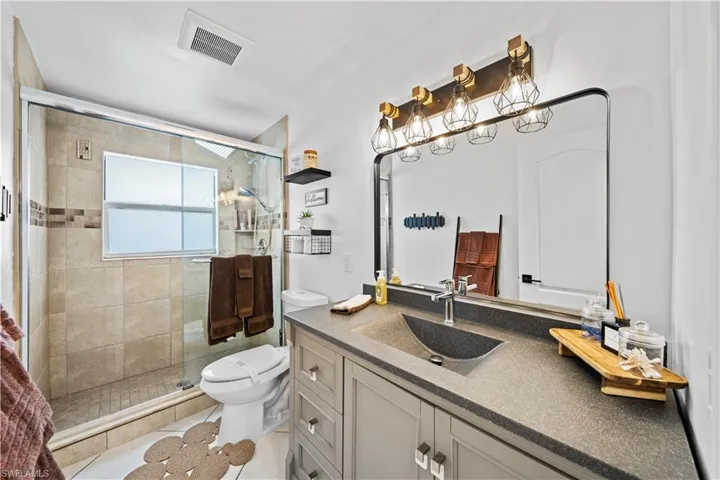 Modern bathroom featuring a glass-enclosed shower with tile surround, a built-in window, and a gray vanity with an integrated sink