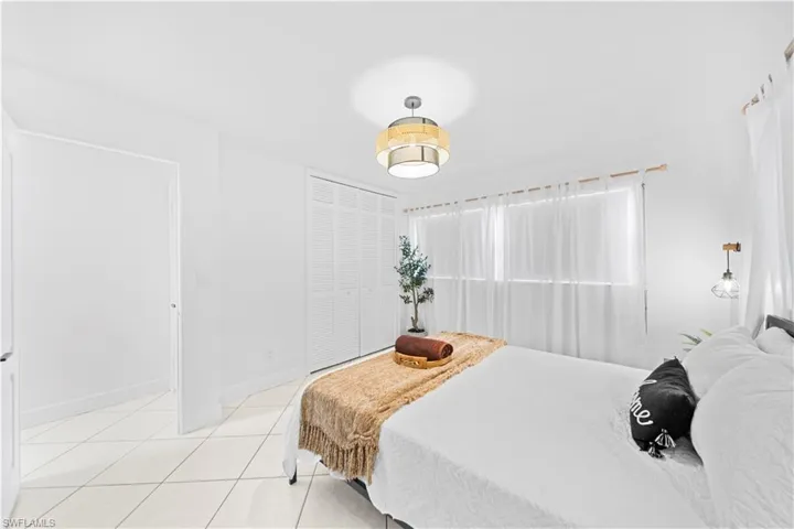 White tile flooring with geometric grout lines, a window featuring sheer white drapery, louvered bi-fold closet doors, a decorative ceiling fixture, and a wall-mounted lighting fixture