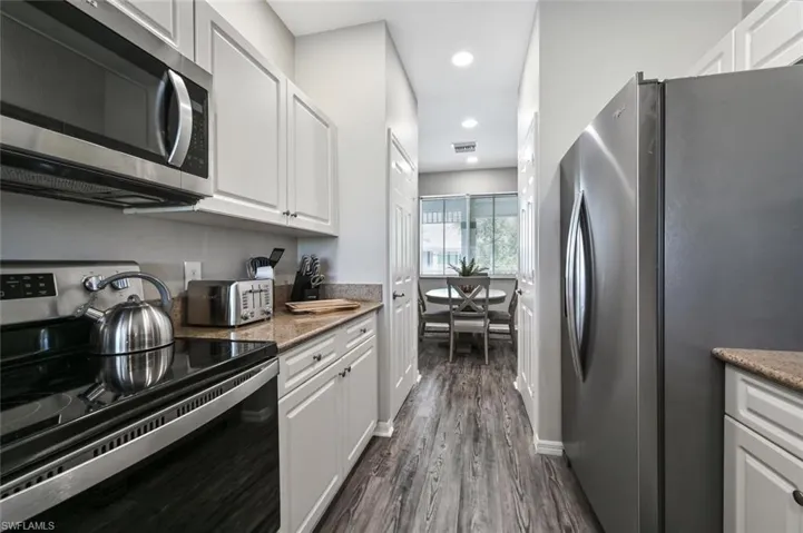 Kitchen with stainless steel appliances, white cabinets, and dark hardwood / wood-style floors