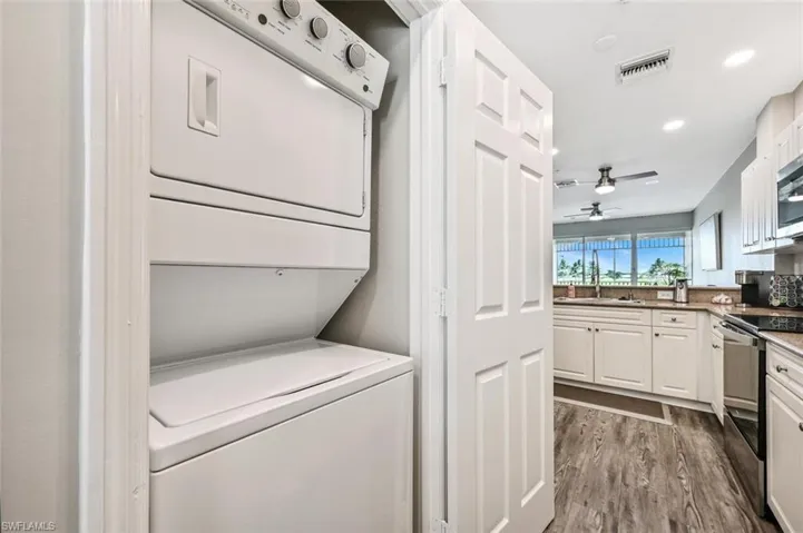 Washroom with stacked washer and clothes dryer, wood-type flooring, ceiling fan, and sink