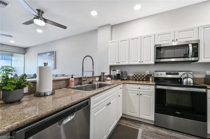 Kitchen featuring white cabinetry, dark wood-type flooring, light stone counters, stainless steel appliances, and ceiling fan