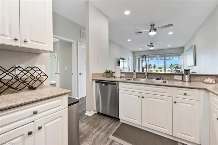 Kitchen featuring ceiling fan, light stone counters, dark wood-type flooring, white cabinetry, and dishwasher