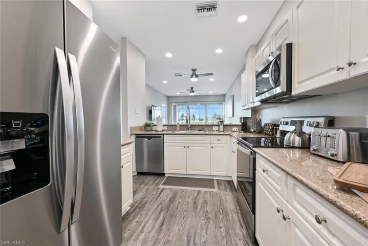 Kitchen with ceiling fan, stainless steel appliances, light wood-type flooring, and white cabinetry
