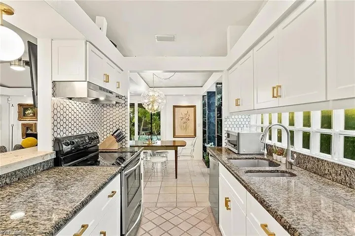 Kitchen featuring appliances with stainless steel finishes, under cabinet range hood, a sink, light tile patterned floors, and backsplash