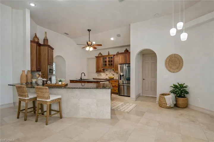 Kitchen with arched walkways, wood finish cabinets, a peninsula, dark stone countertops, and tasteful backsplash