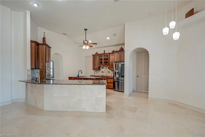 Kitchen featuring arched walkways, dark stone countertops, a center island, wood finish cabinetry, and decorative backsplash