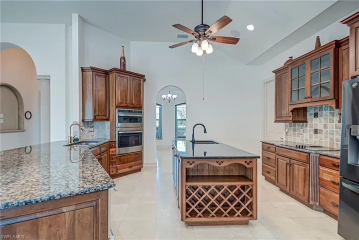 Kitchen with tasteful backsplash, dark stone countertops, arched walkways, lofted ceiling, and glass insert cabinets