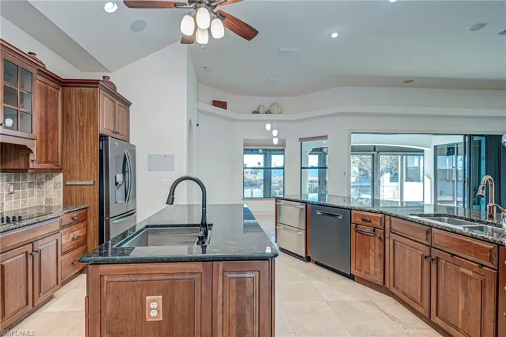 Kitchen with dark stone countertops, wood finish cabinetry, and an island with sink