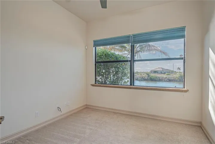Spare room featuring light carpet, a water view, and a ceiling fan