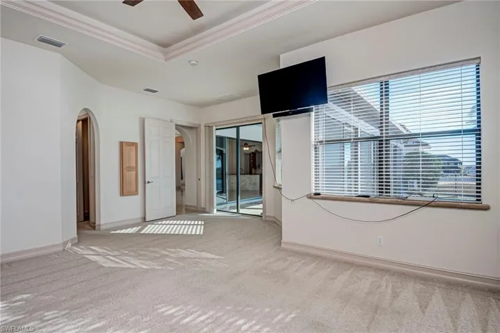 Unfurnished room featuring arched walkways, a ceiling fan, light carpet, a tray ceiling, and ornamental molding