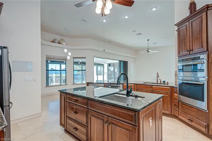 Kitchen with dark stone counters, ceiling fan, a kitchen island with sink, stainless steel appliances, and wood finish cabinets