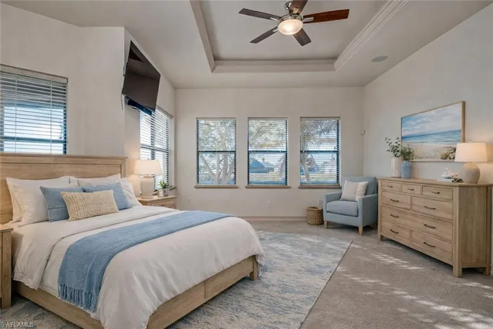 Carpeted bedroom featuring a ceiling fan and a tray ceiling
