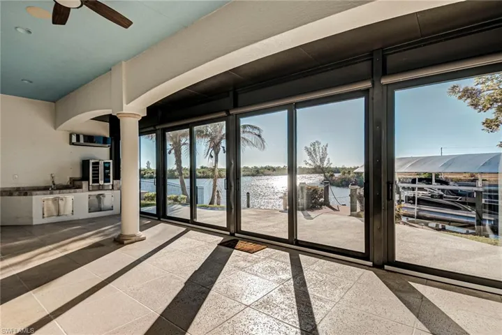 Unfurnished living room featuring ornate columns, a ceiling fan, a water view, beverage cooler, and arched walkways