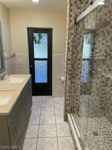 Full bathroom featuring double vanity, a shower stall, light tile patterned floors, tile walls, and wainscoting