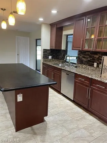 Kitchen featuring a center island, dark stone counters, dishwasher, backsplash, and glass insert cabinets