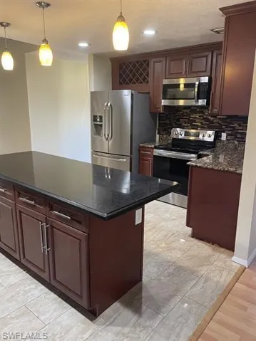 Kitchen with pendant lighting, stainless steel appliances, a kitchen island, dark stone countertops, and decorative backsplash