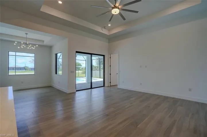 Empty room with ceiling fan with notable chandelier, a high ceiling, hardwood / wood-style floors, and a tray ceiling