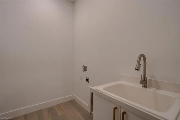 Laundry area with hookup for a washing machine, light hardwood / wood-style floors, electric dryer hookup, and sink