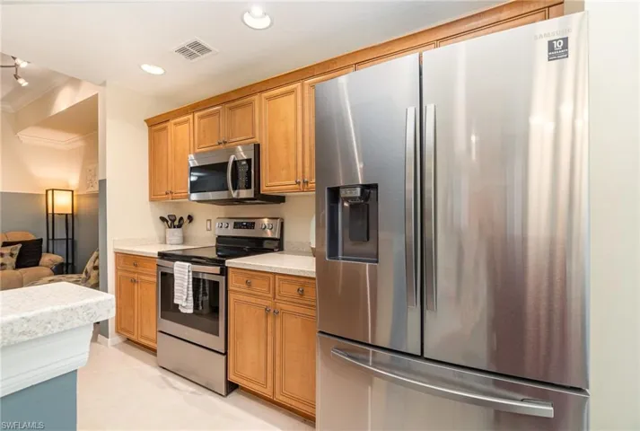 Kitchen with light stone countertops, crown molding, and appliances with stainless steel finishes