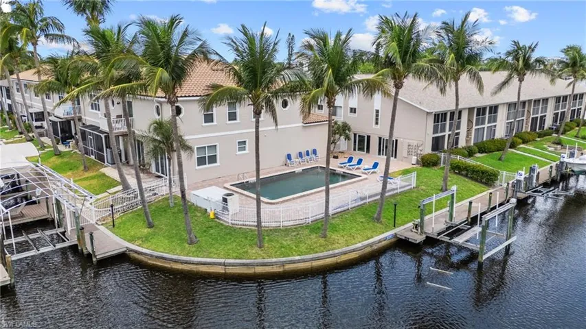 Rear view of house featuring fence, boat lift, stucco siding, a water view, and a yard