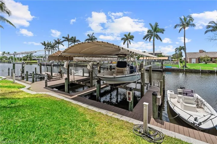 View of dock featuring boat lift, a water view, and a yard