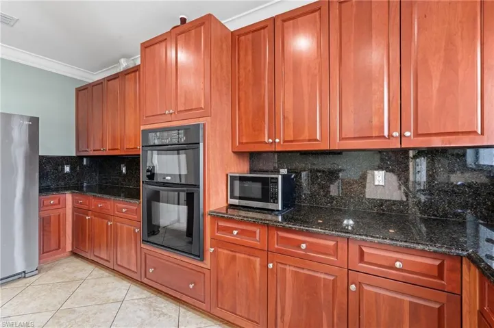 Kitchen featuring crown molding, decorative backsplash, dark stone counters, light tile patterned floors, and stainless steel appliances