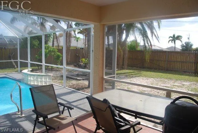 Screen enclosed Lanai with pool and fenced backyard with lots of palm trees.