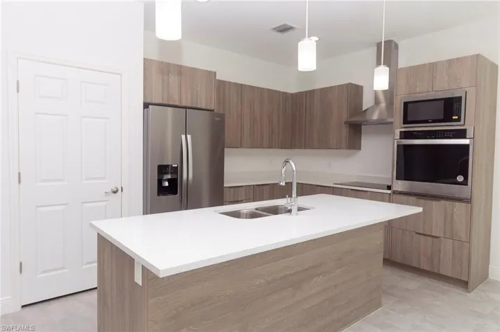 Kitchen with sink, decorative light fixtures, black appliances, and a center island with sink