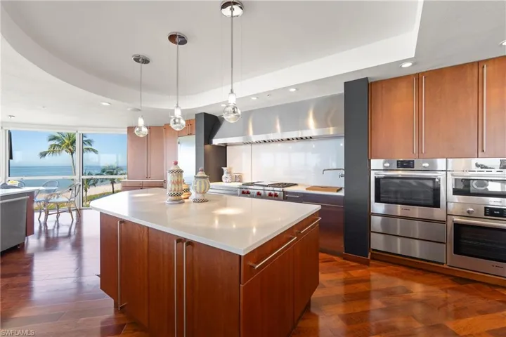 Kitchen with recessed lighting, brown cabinets, decorative light fixtures, a kitchen island, and a tray ceiling