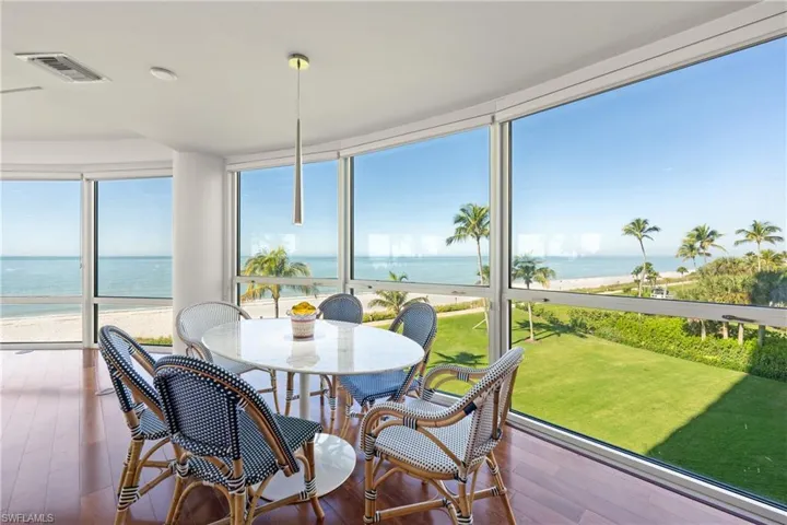 Sunroom with view of water and beach, a wall of windows, and hardwood / wood-style floors